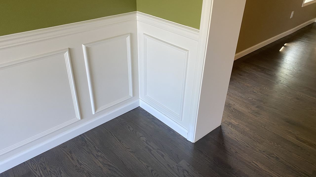 Dark stained hardwood floor meeting white raised panel wainscoting in a finished room