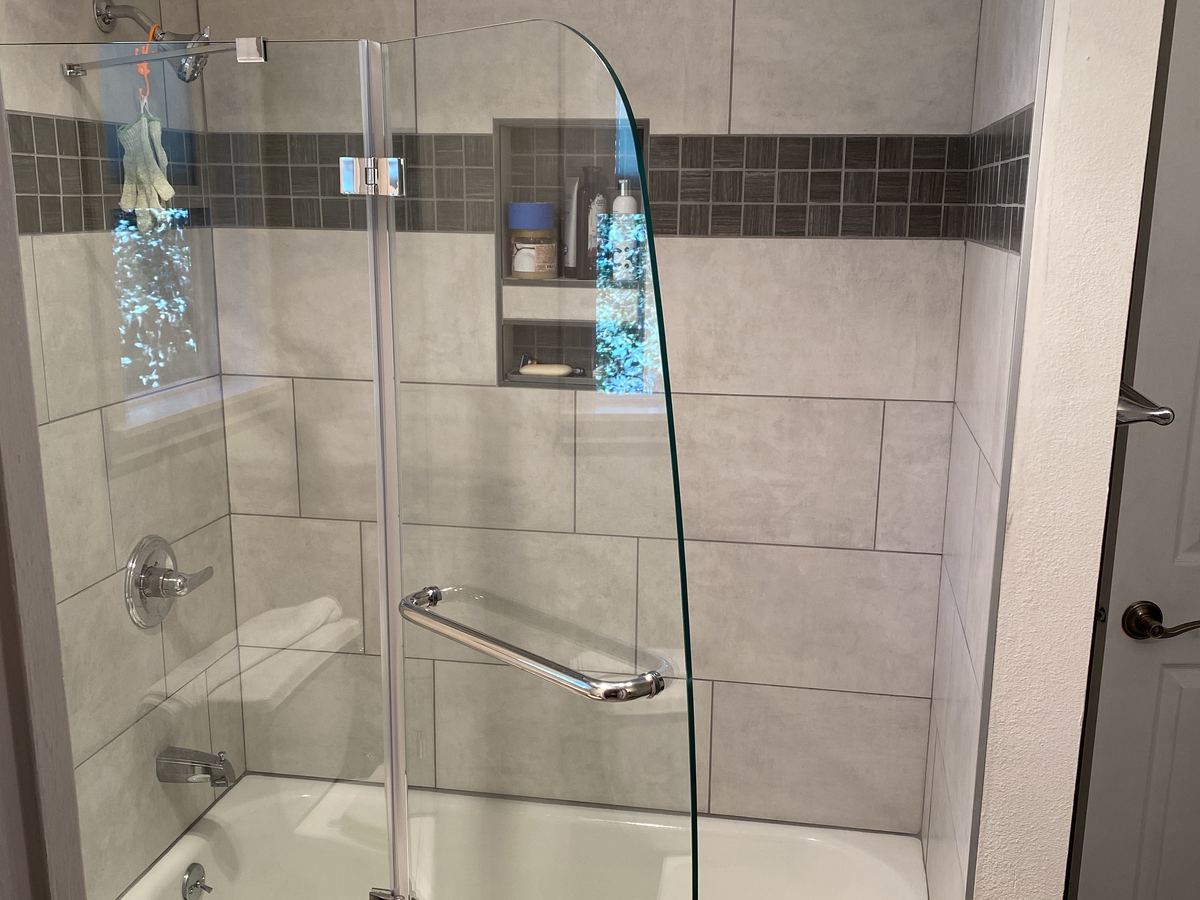 Finished tub and shower with large gray wall tile, a mosaic accent band and a glass door