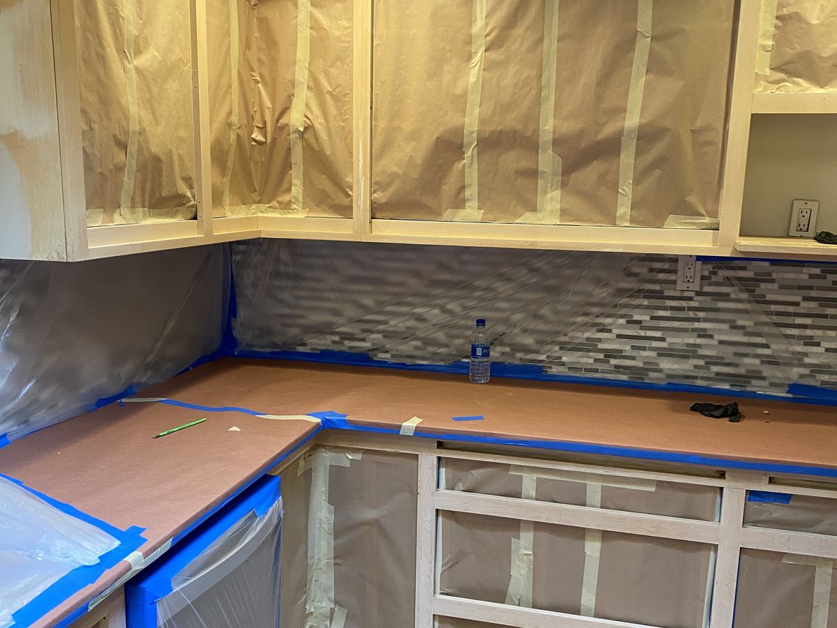 Kitchen remodel in progress, with new cabinets masked for finishing and a glass mosaic tile backsplash