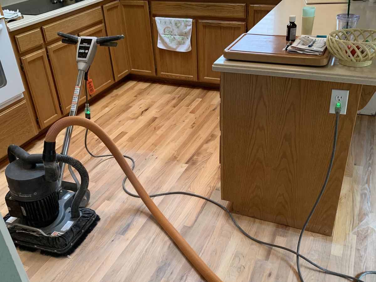 Floor sander on a freshly sanded oak floor in a kitchen with wood cabinets